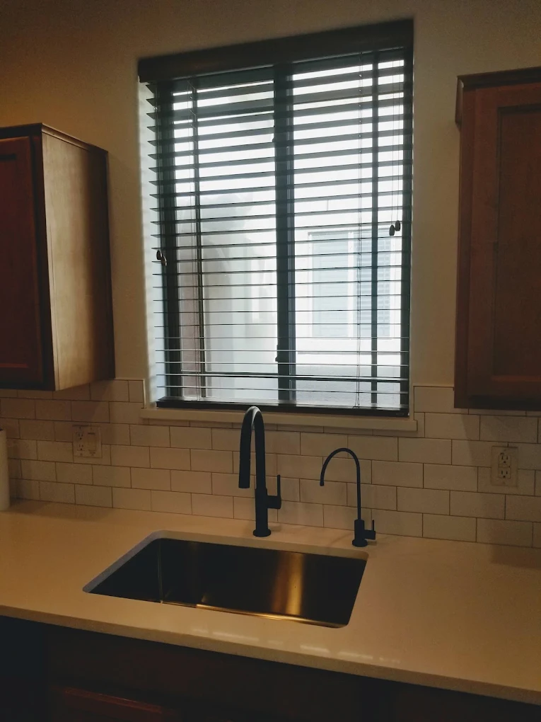 Modern kitchen sink with black faucet and window shutters above