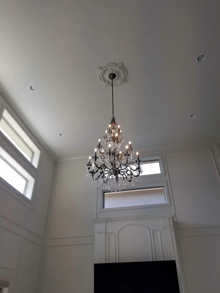 Ornate crystal chandelier hanging from decorative ceiling medallion in bright foyer with white walls and transom window